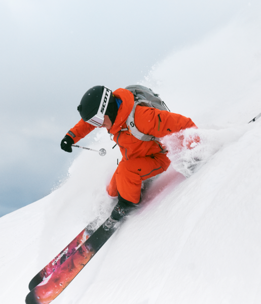 Freerider in oranger Jacke fährt im Tiefschnee einen steilen Hang hinab