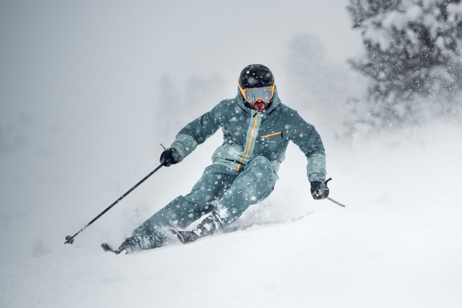 Skifahrer in Petrol fährt im Schneetreiben über die Piste